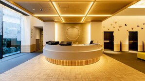 A modern reception area with a circular desk, a large window, and a wall with abstract art. - Montblanc Hotel RAFFINE NAGOYA EKIMAE (Nagoya)