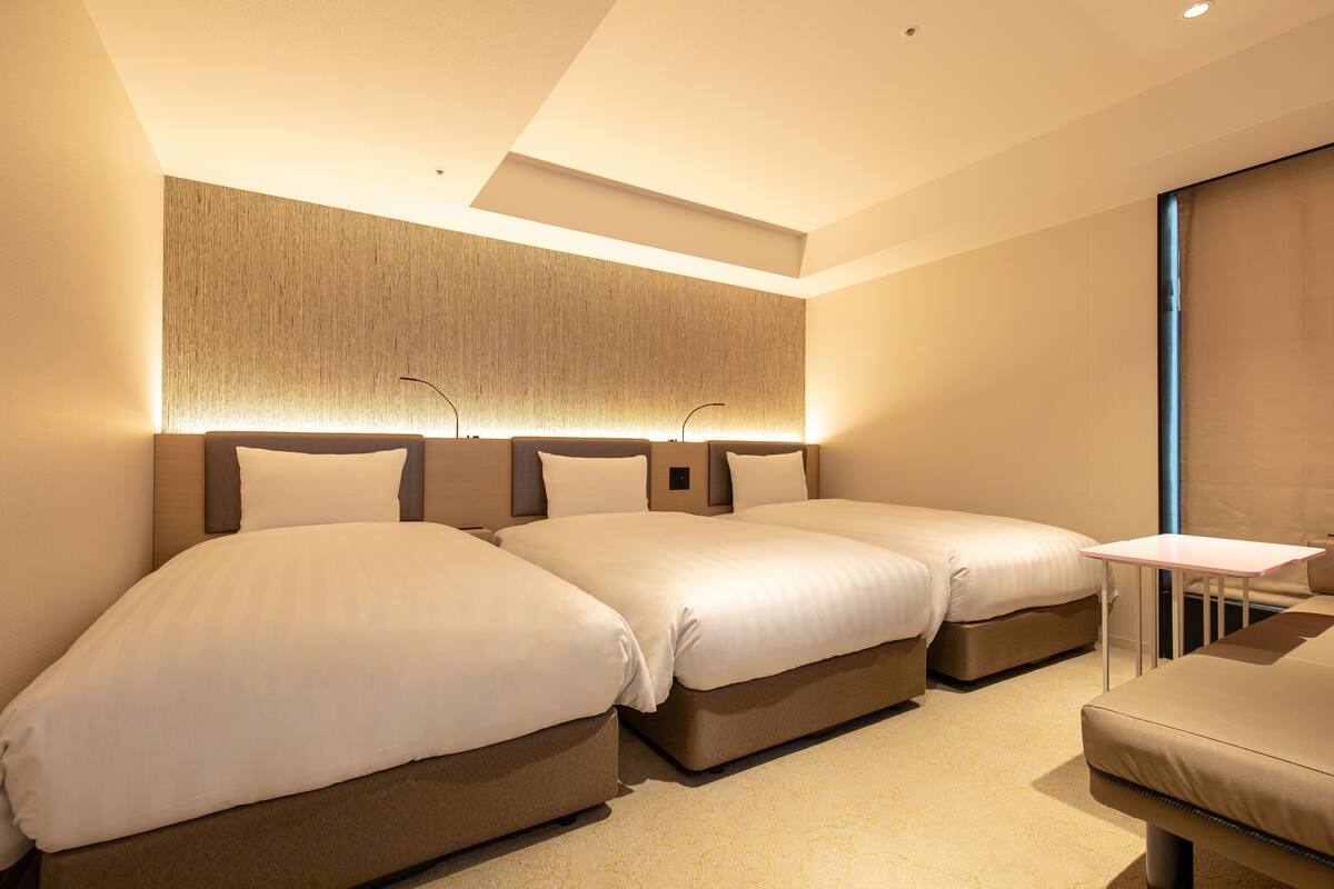A hotel room with two beds, a small table, and a large window.