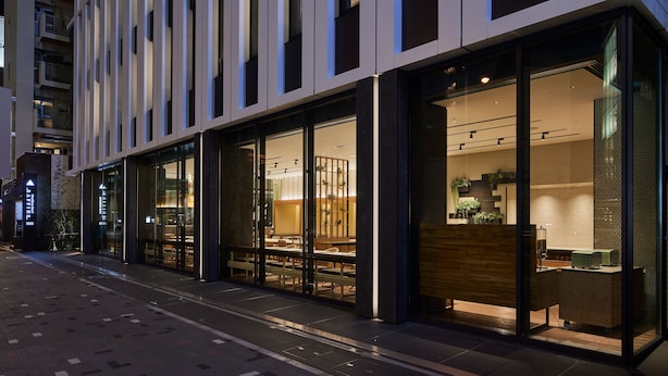 A modern building with large glass windows, a visible seating area with tables and chairs, and a reception desk. - Montblanc Hotel RAFFINE NAGOYA EKIMAE (Nagoya)
