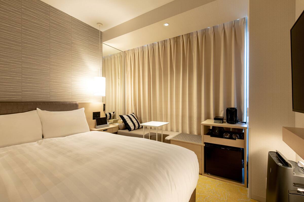 A hotel room with a large bed, a desk, a chair, a coffee machine, and a TV.