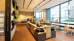 A modern cafe with a central counter, seating area, and large windows offering a view of the street. - Montblanc Hotel RAFFINE NAGOYA EKIMAE (Nagoya)