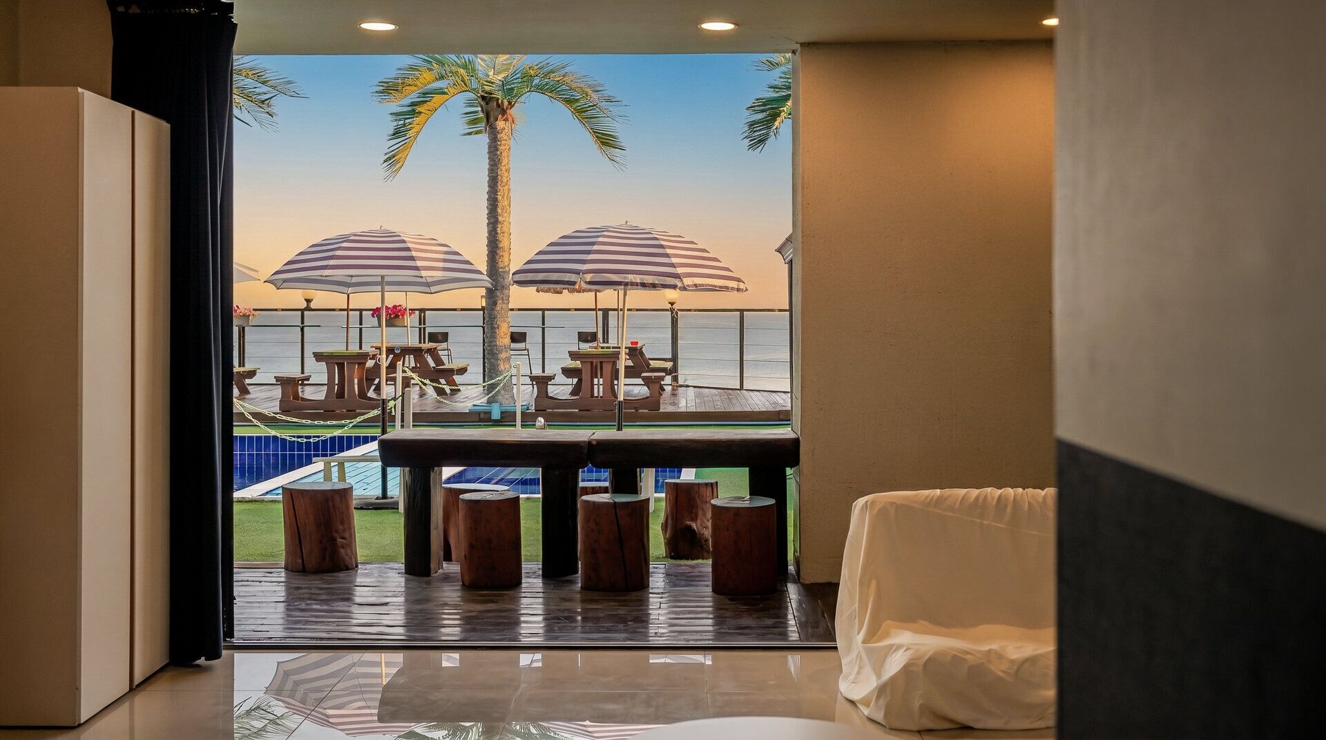A room with a view of a pool area, including tables and umbrellas.