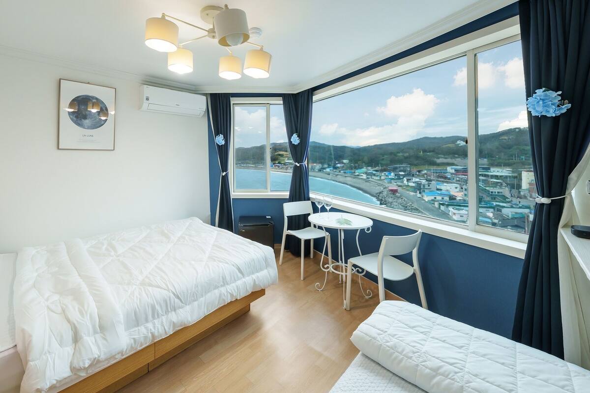 A hotel room with a bed, a small table with chairs, a view of the sea, and a framed picture on the wall.