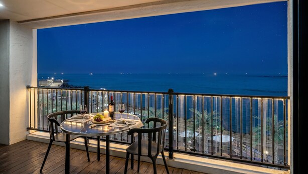 A balcony with a table set for two, overlooking a coastal view at night. - Gyeongju Neulsiwon Pension (Gyeongju)