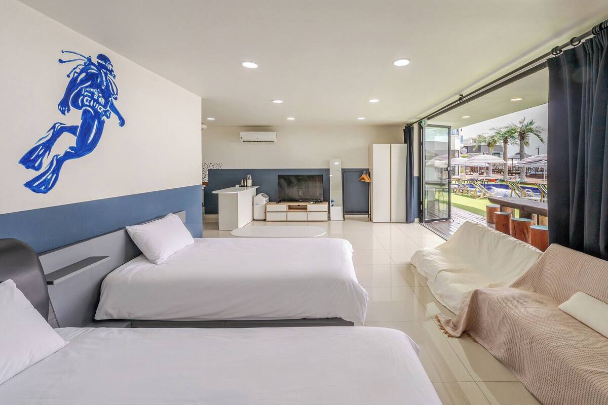 A hotel room with two beds, a TV, a kitchenette, and a balcony with outdoor seating.