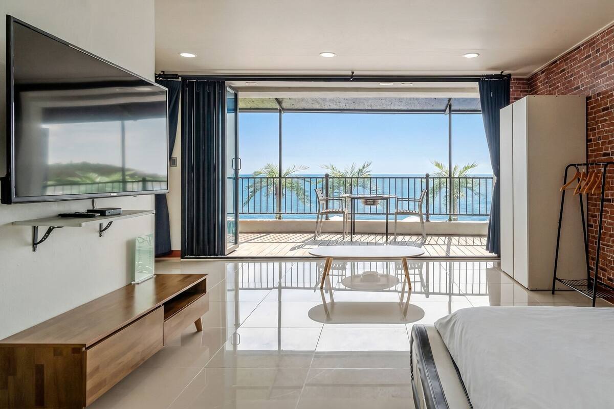 A modern hotel room with a balcony, a TV, a wooden cabinet, and a bed.