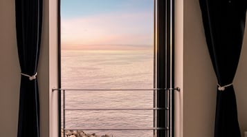 Una ventana con vista al mar, cortinas recogidas y una barandilla de metal.