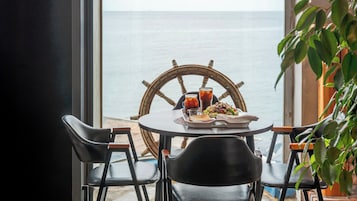 Una mesa con sillas, una rueda de barco y una comida junto a una ventana con vista al mar.