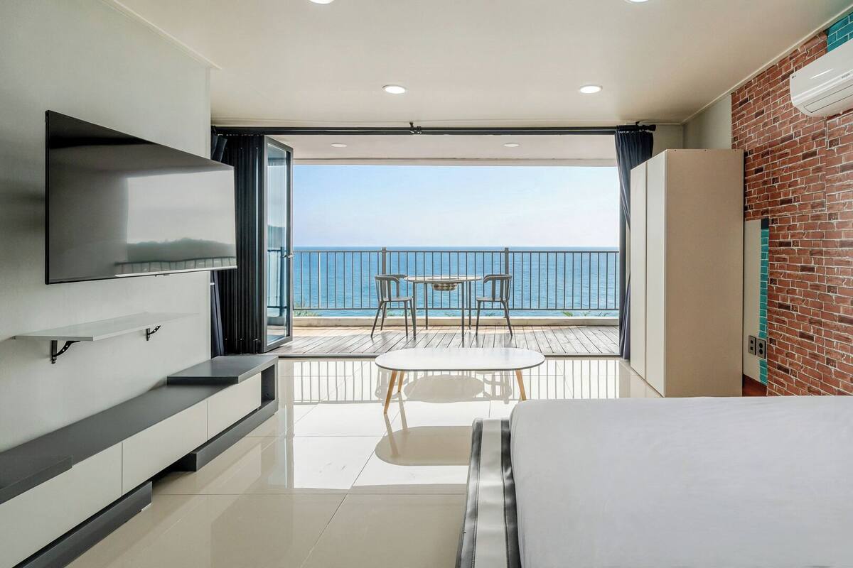 A modern hotel room with a balcony, a flat-screen TV, and a brick wall.