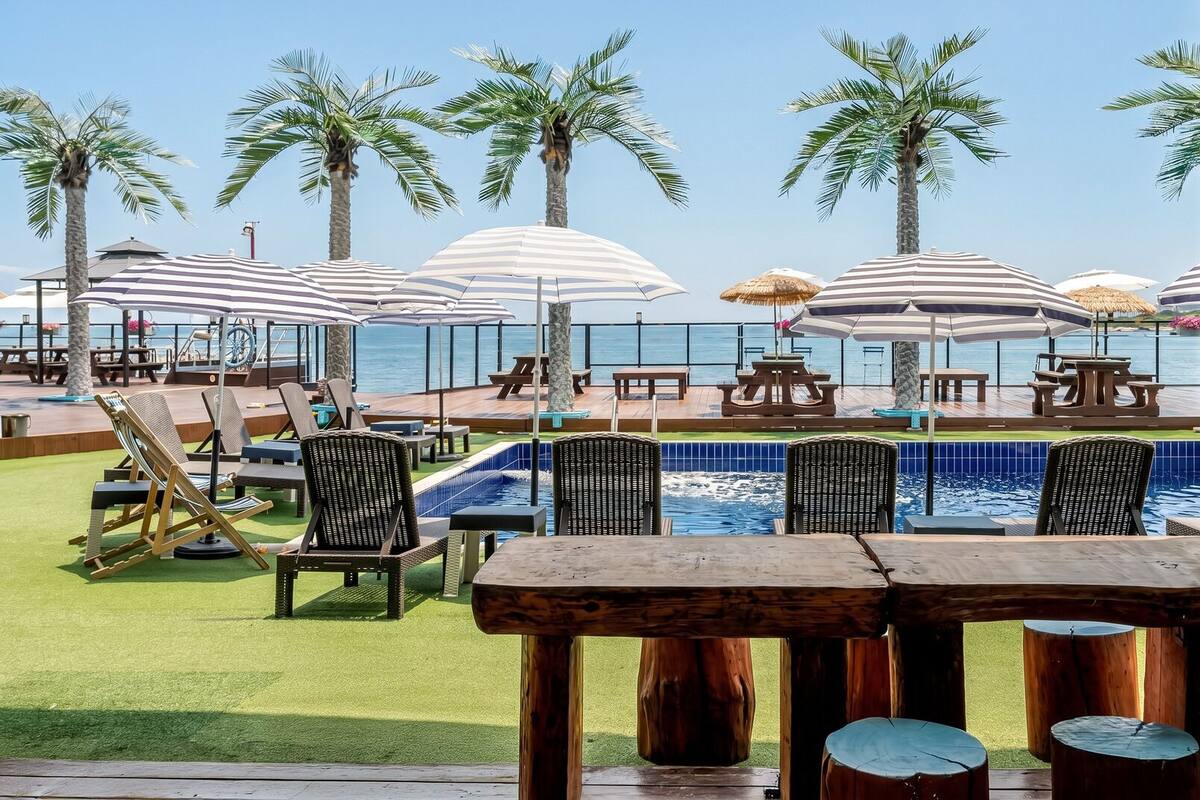 A poolside area with lounge chairs, umbrellas, and a view of the ocean.