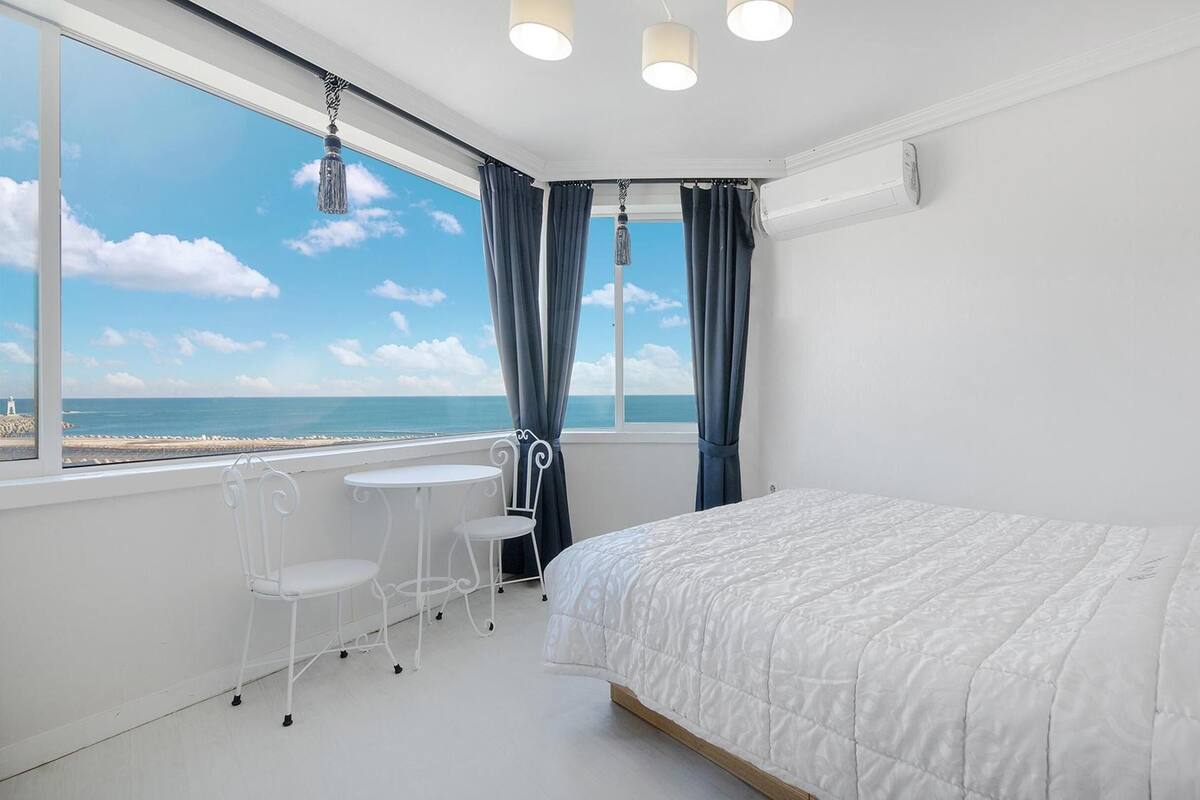 A bedroom with a large window, a bed, a small table, and chairs.