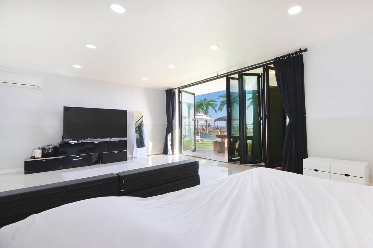 A modern hotel room with a large bed, a flat-screen TV, a TV stand, and a sliding glass door leading to an outdoor area.