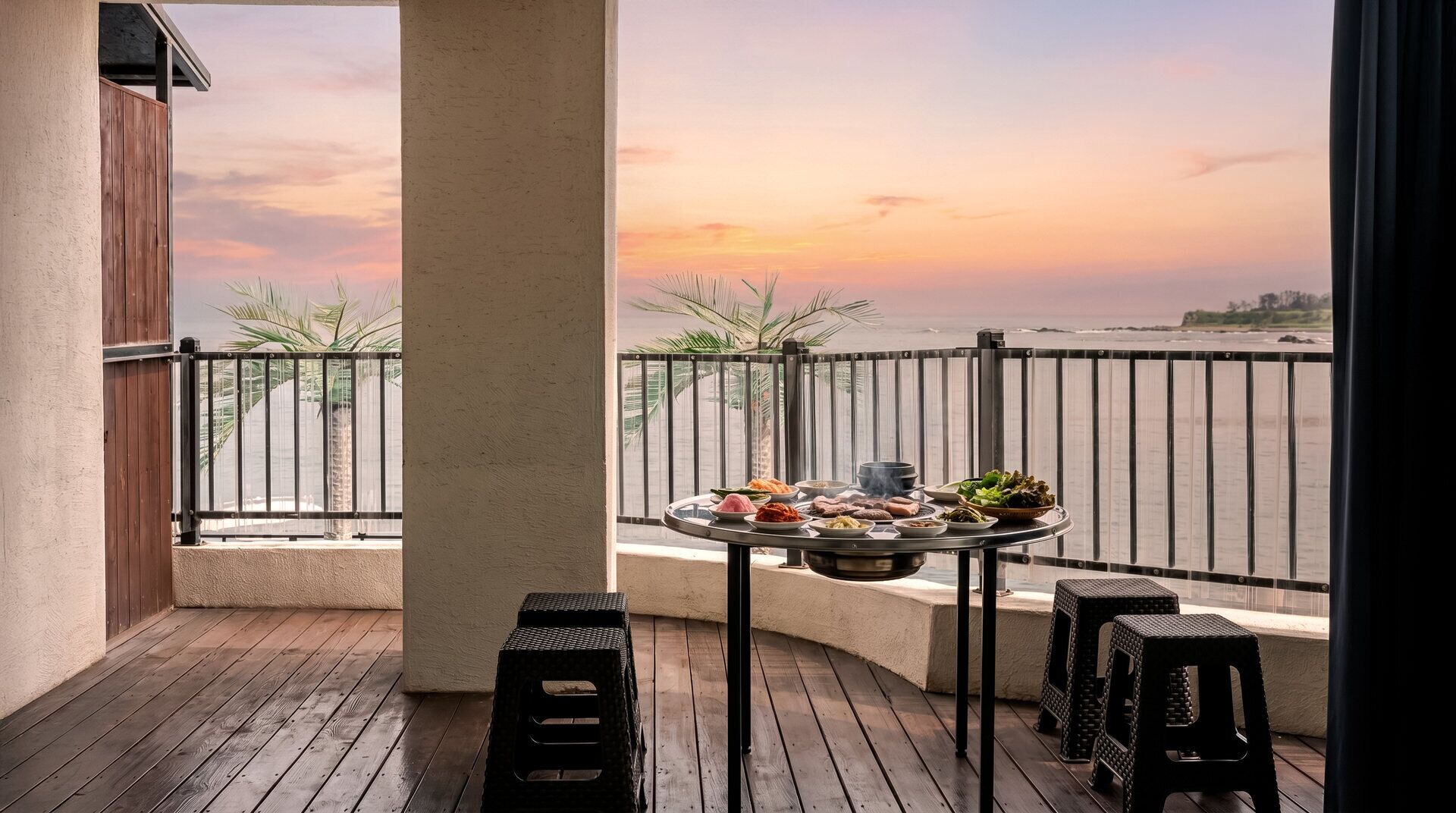 A balcony with a table set for a meal, overlooking a beach at sunset.