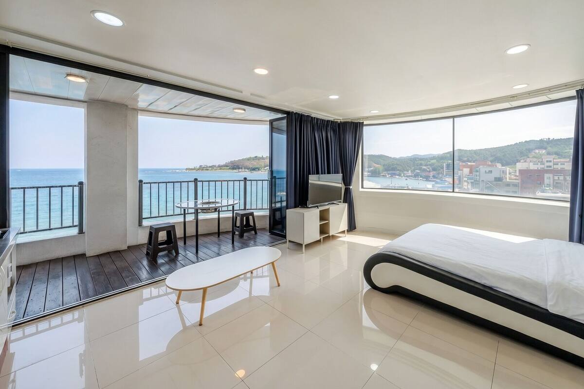 A modern hotel room with a balcony, a bed, a TV, and a dining area.