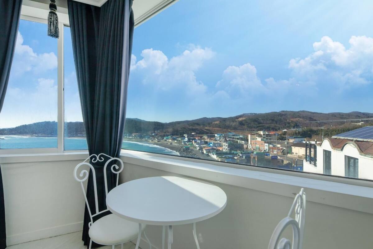 A room with a view of a coastal town, a small round table, and a chair.