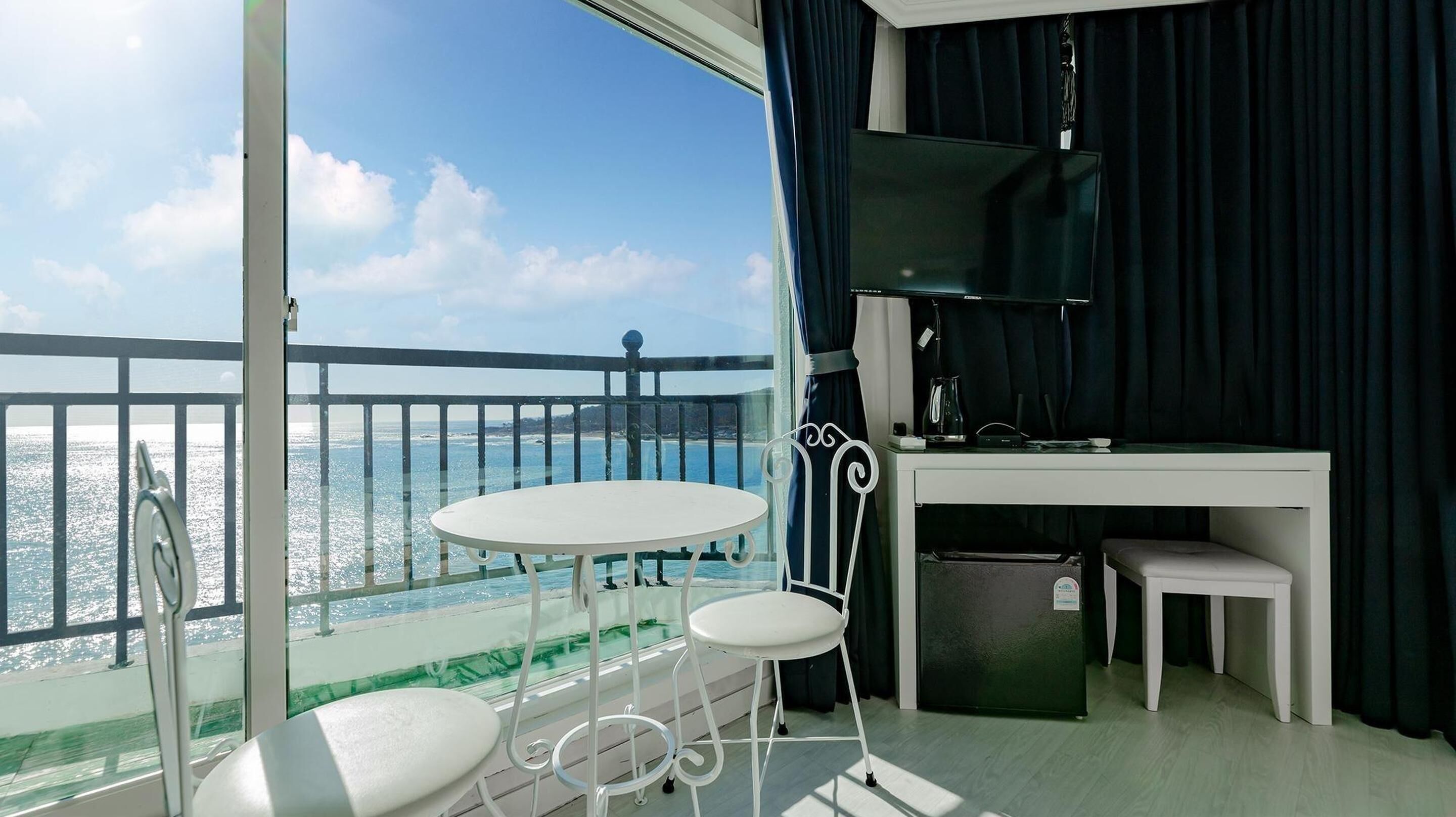 A balcony with a white table and two chairs, a small desk with a chair, and a view of the sea.