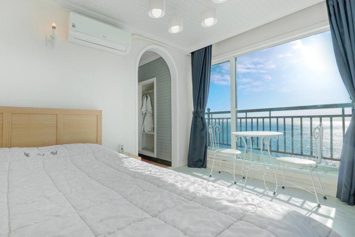 A bedroom with a large bed, an air conditioning unit, a walk-in closet, and a balcony with a view of the sea.