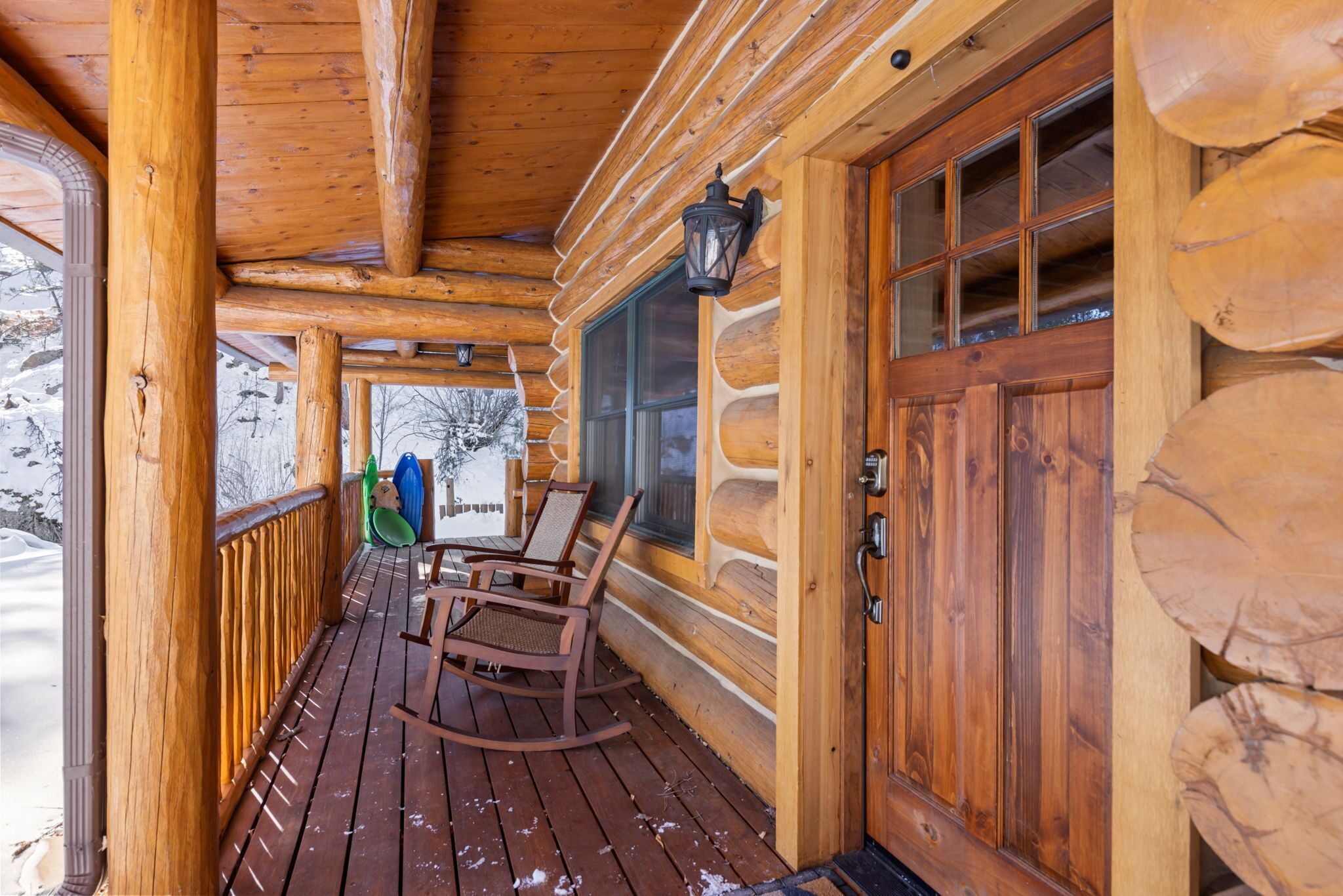 Une cabane en rondins de bois dotée d’un porche avec des fauteuils à bascule et d’une porte en bois avec des panneaux de verre.