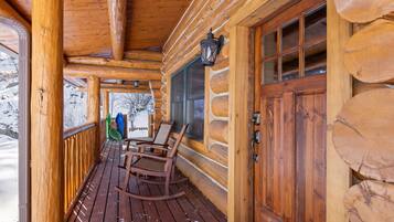 Une cabane en rondins de bois dotée d’un porche avec des fauteuils à bascule et d’une porte en bois avec des panneaux de verre.