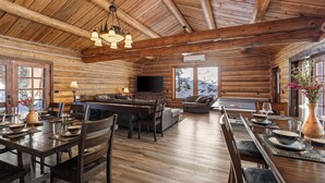 Interior de uma cabana de madeira com sala de jantar, sala de estar e lareira.