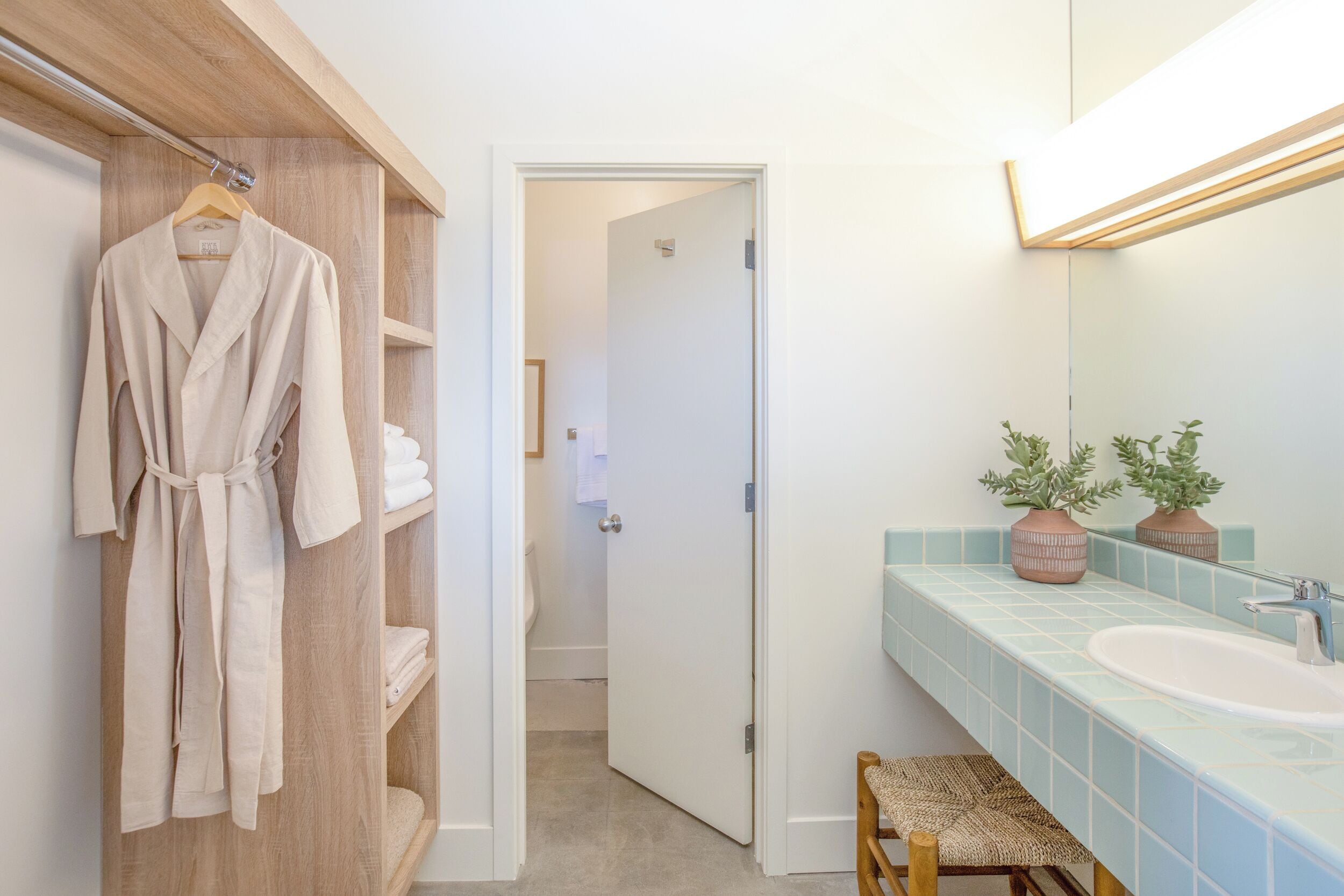 Un baño con un perchero de madera, un lavamanos con azulejos azules y un espejo con una lámpara.