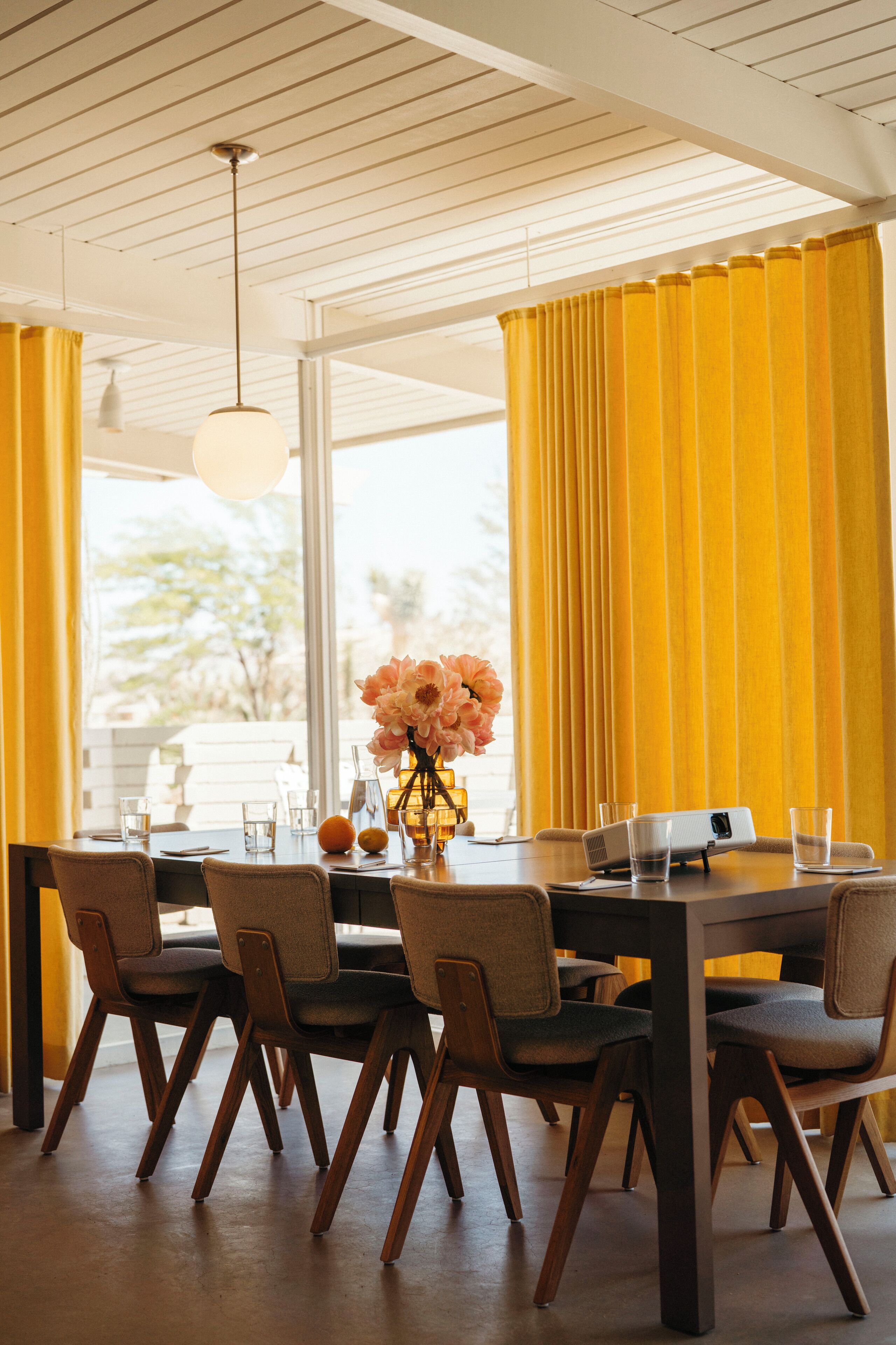 A dining area with a table set for four, a projector, and a vase with flowers.
