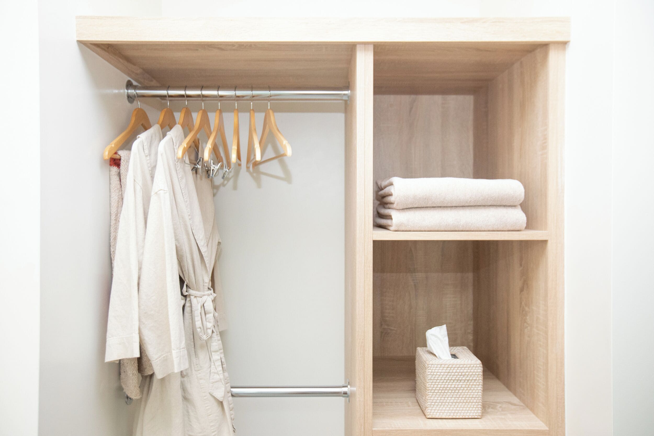 Een houten kast met galg voor gewassen en een plank met opgevouwen handdoeken en een zakdoos.