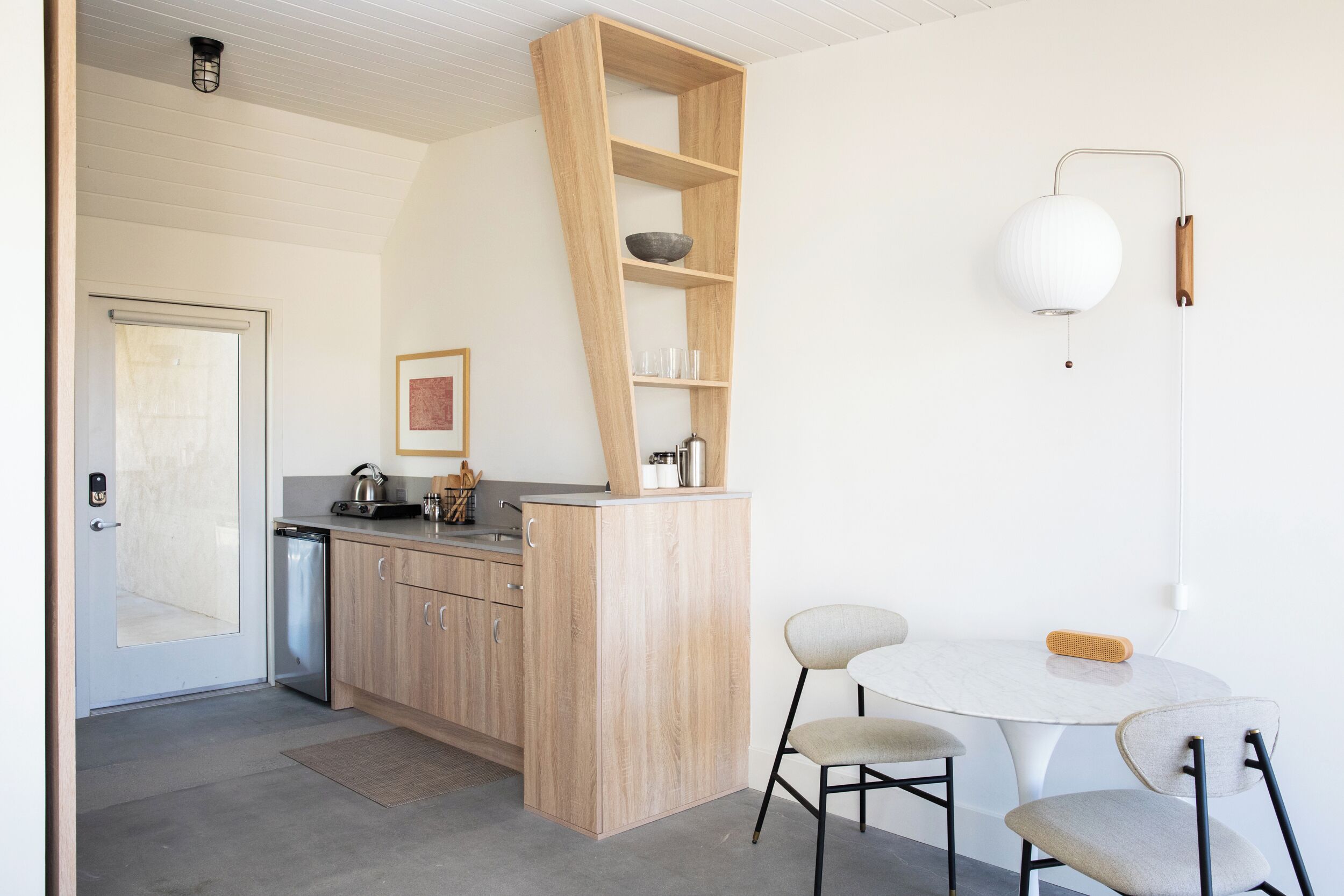 Una cocina moderna con armarios de madera, una estantería empotrada, una mesa redonda con dos sillas y una lámpara de pared.