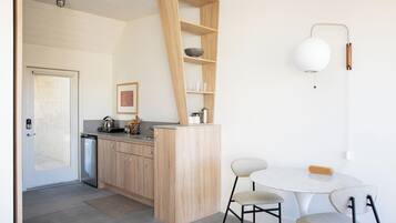Una cocina moderna con armarios de madera, una estantería empotrada, una mesa redonda con dos sillas y una lámpara de pared.