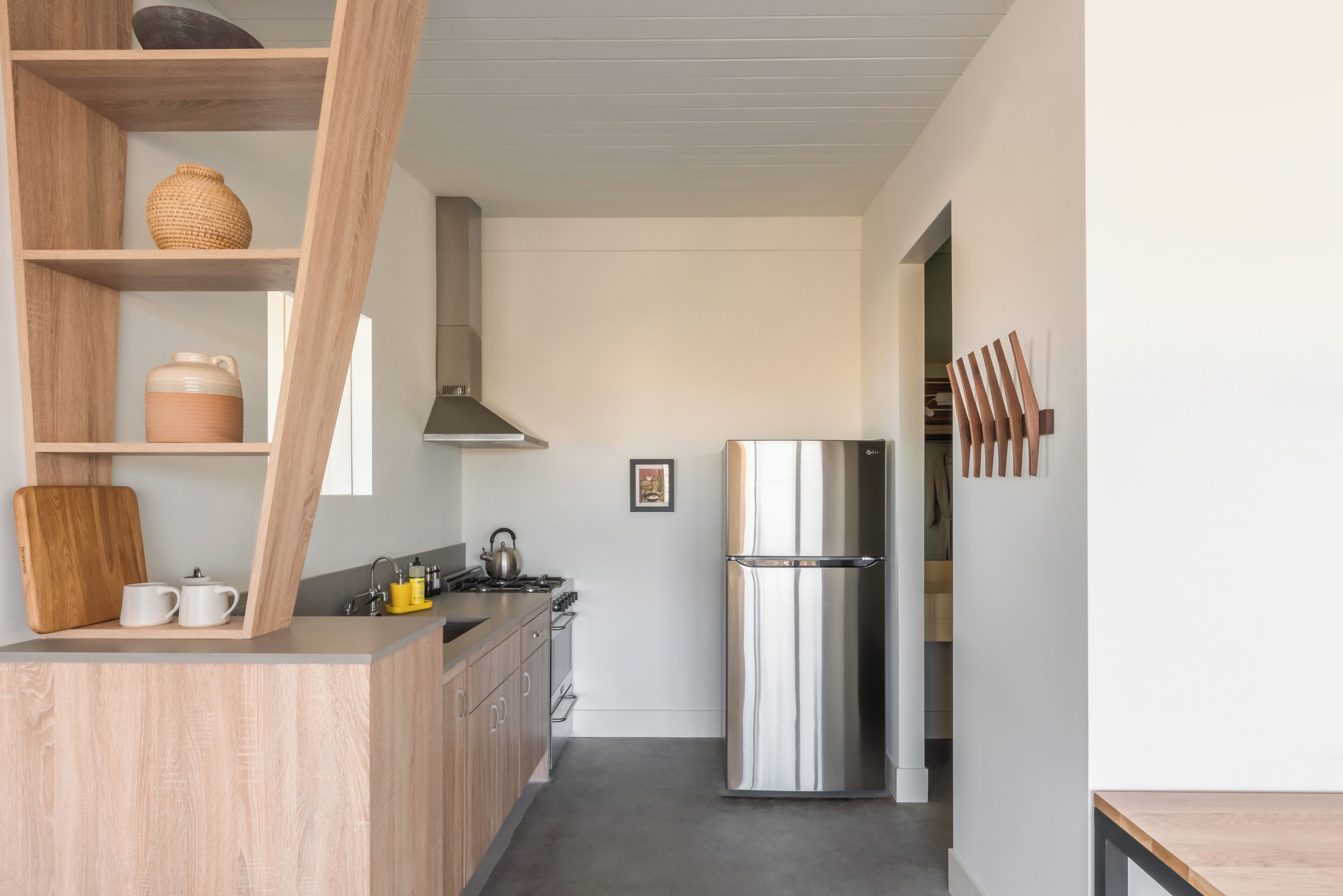 A modern kitchen with wooden cabinets, a stainless steel refrigerator, and a wooden shelf with kitchenware.