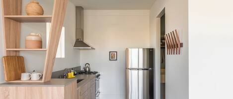 A modern kitchen with wooden cabinets, a stainless steel refrigerator, and a wooden shelf with kitchenware.