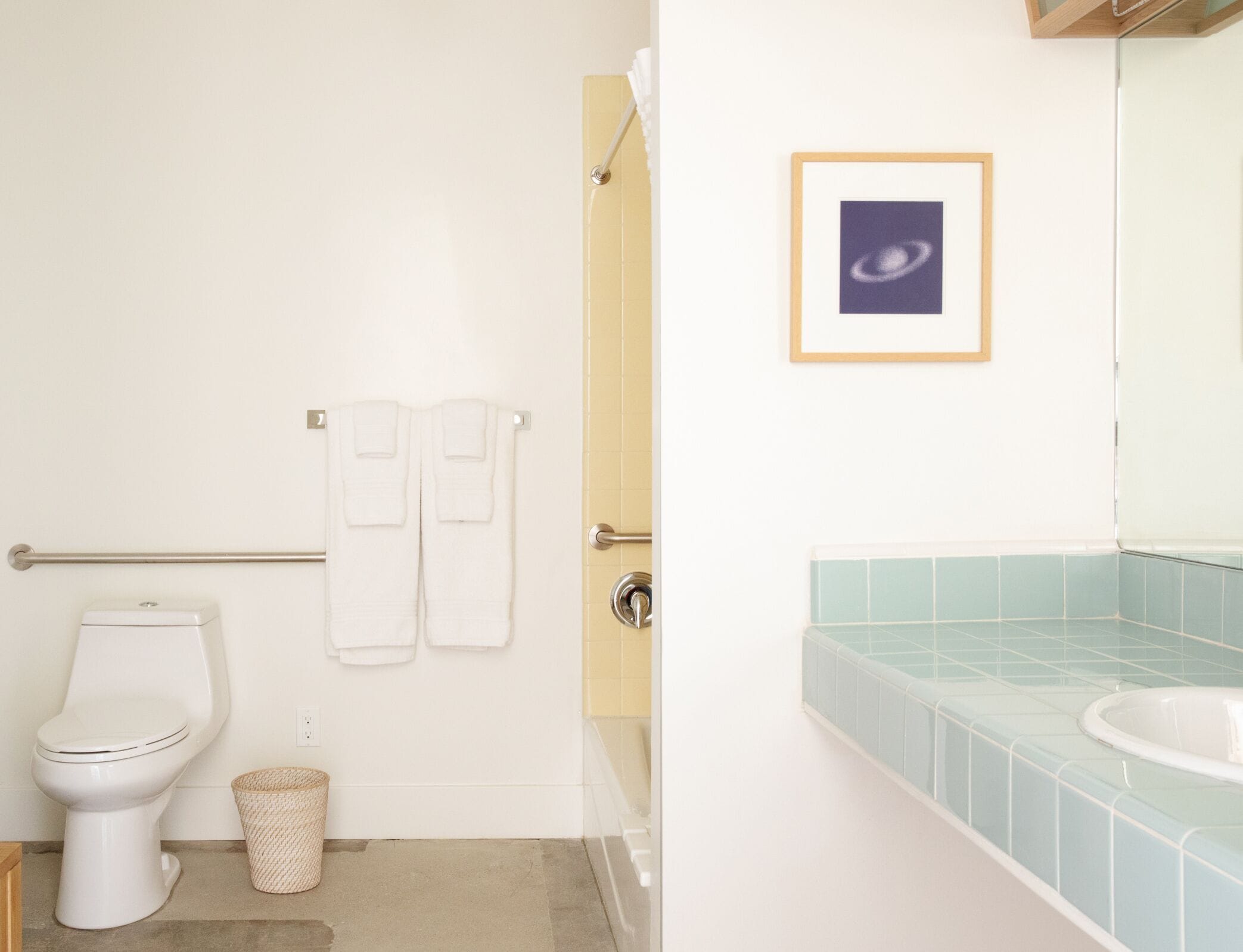 Un baño con inodoro, dos toallas, un cuadro enmarcado y un lavamanos con azulejos azules.