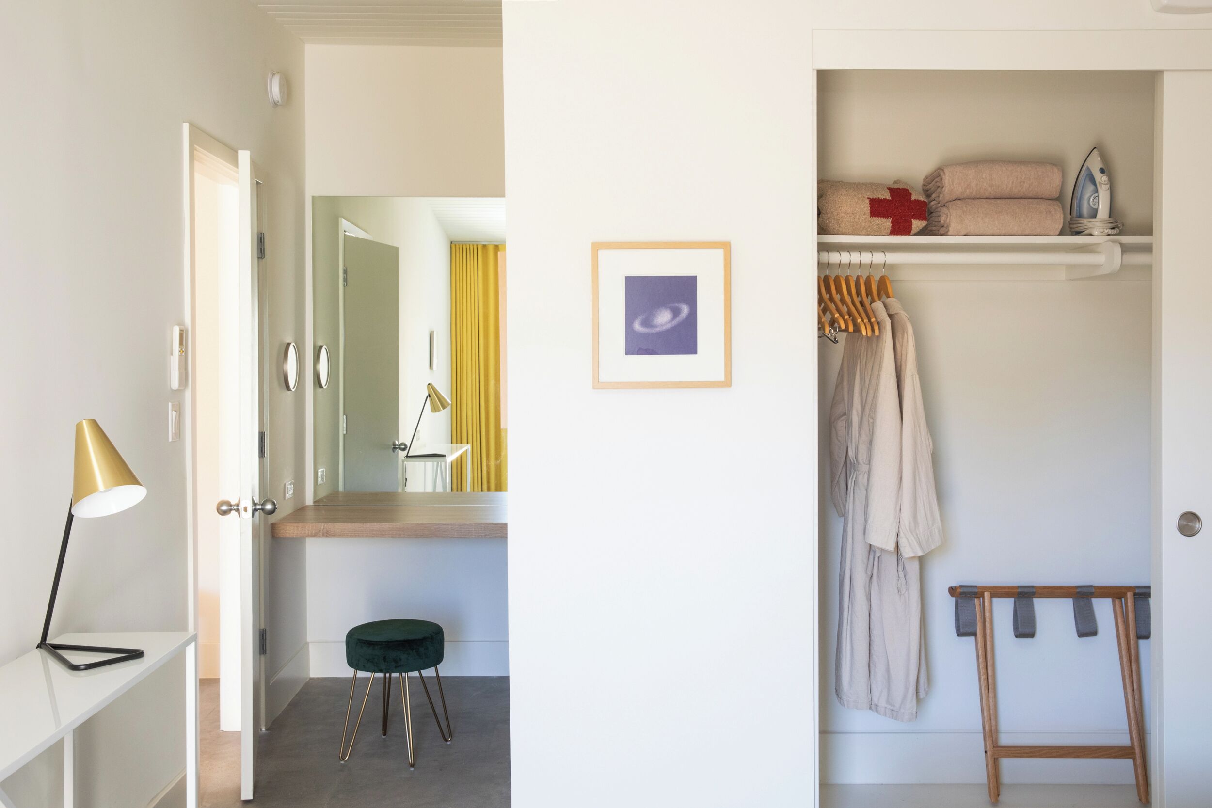Et moderne badeværelse med et toiletbord, en skammel, et spejl og en hylde med håndklæder og et strygejern.