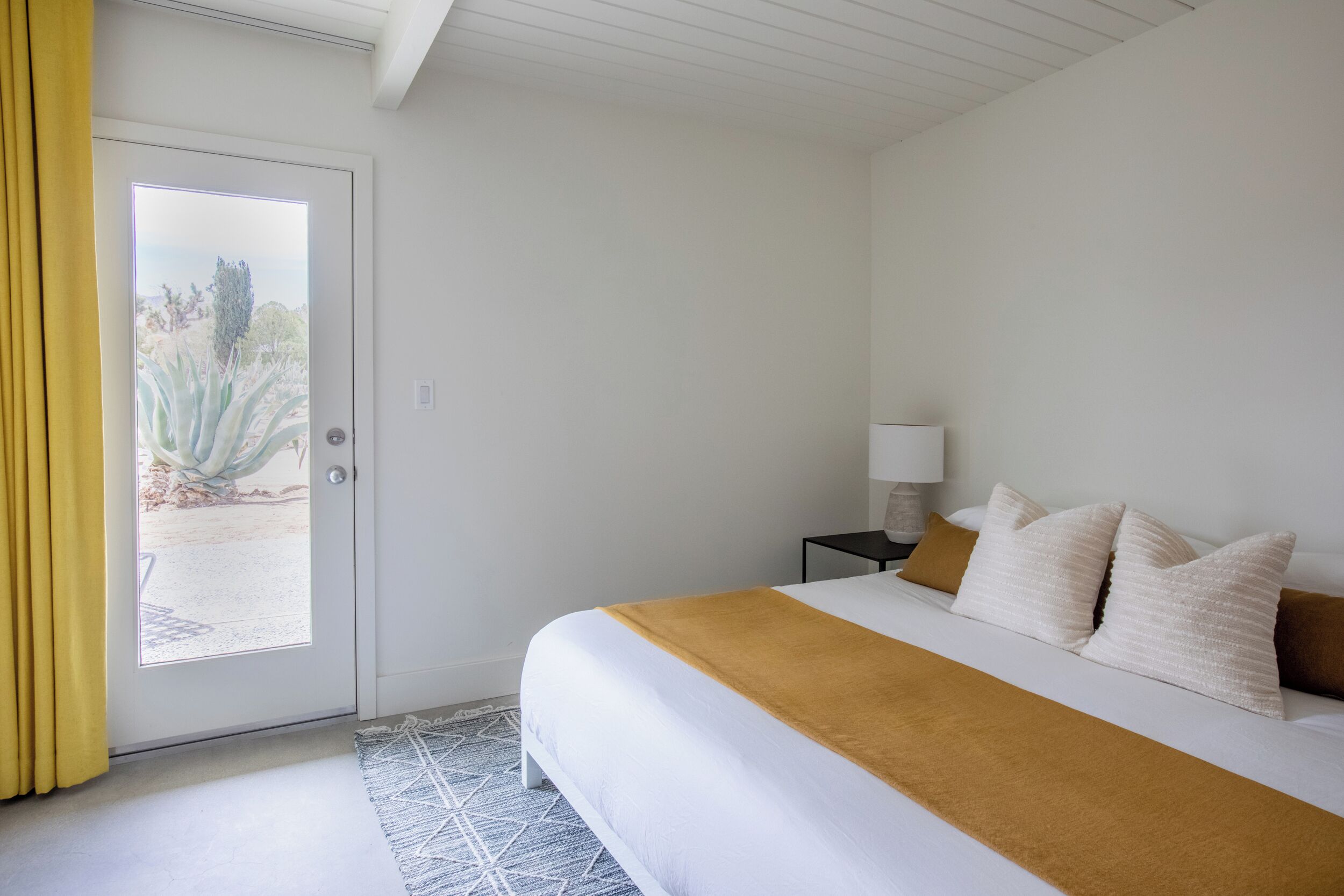 A bedroom with a bed, a nightstand, a lamp, and a view through a door.