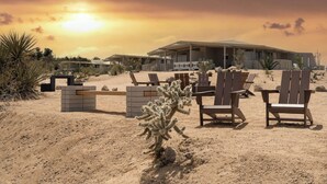 A desert landscape with a modern building, desert plants, and several wooden chairs. - The Bungalows by Homestead Modern at The Joshua Tree Retreat Center (Joshua Tree)