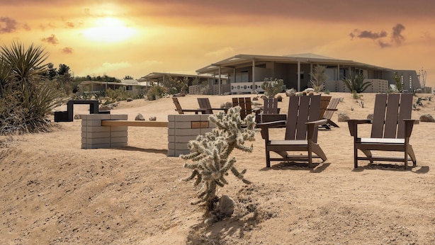 Paesaggio desertico con un edificio moderno, piante tipiche del deserto e diverse sedie di legno.