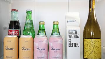 Une étagère de réfrigérateur contenant diverses boissons, notamment des canettes de soda « Recess » et « Terrier », une bouteille de vin et un emballage de « Boxed Water ».