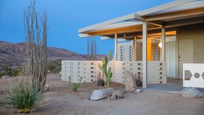 Una casa moderna con patio coperto, piante tipiche del deserto e montagne sullo sfondo.