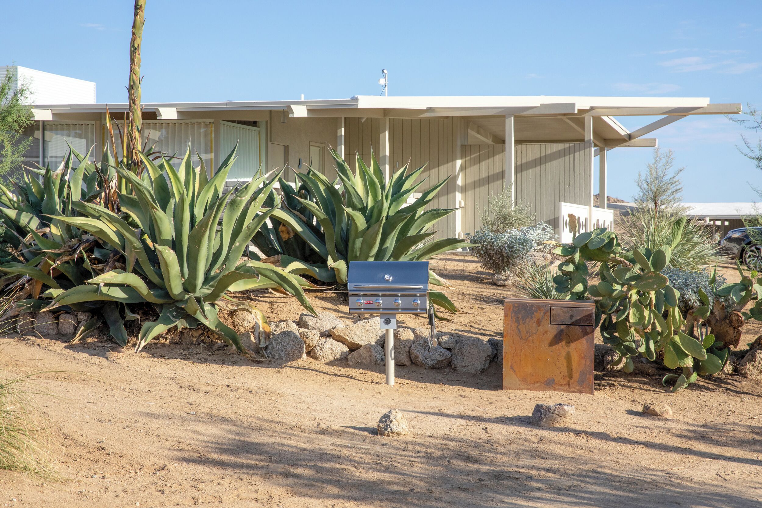 A modern house with a covered patio, surrounded by desert vegetation.