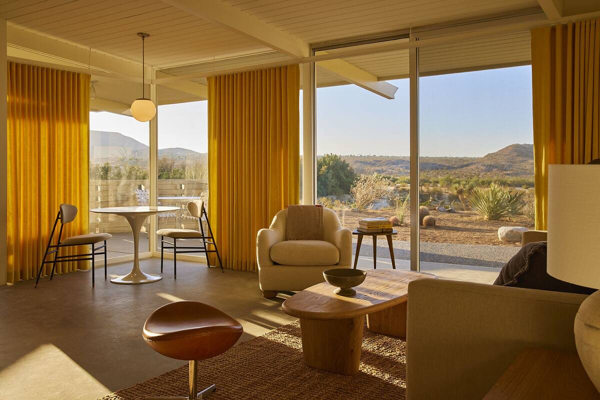 Ein modernes Wohnzimmer mit großen Fenstern, einem Essbereich und Blick auf eine Wüstenlandschaft.