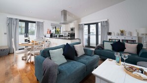 Una sala moderna con un juego de sofá color turquesa, un comedor con mesa blanca y una cocina al fondo.