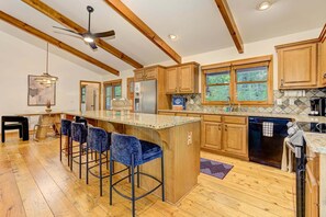 Une cuisine avec des meubles en bois, un îlot central doté de tabourets, un ventilateur de plafond et un lave-vaisselle.