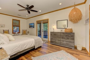 Une chambre à coucher comprenant un lit, une commode, un ventilateur de plafond, un téléviseur et une porte-fenêtre donnant sur un balcon.