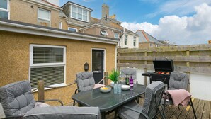 An outdoor patio with a table, chairs, a grill, and a view of neighboring houses. - Porthmeor View, St Ives  – Sleeps 8 – On-Site Parking for Two Cars – Sea Views (St Ives)