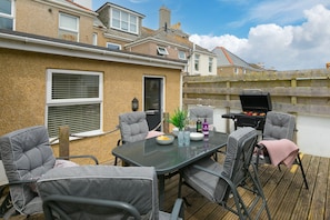 An outdoor patio with a table, chairs, a grill, and a view of neighboring houses.