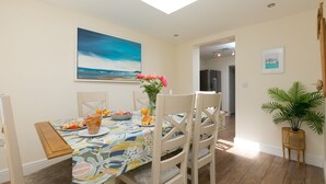 A dining area with a table set for two, a painting above, and a plant on the side. - Porthmeor View, St Ives  – Sleeps 8 – On-Site Parking for Two Cars – Sea Views (St Ives)