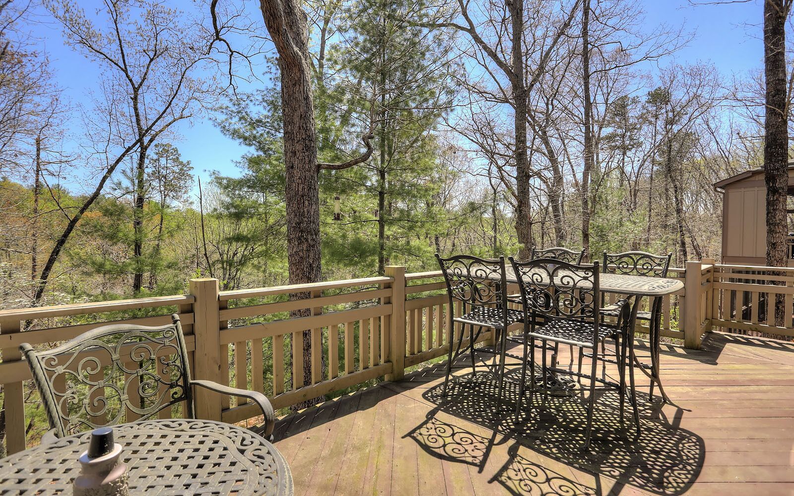 A wooden deck with metal outdoor furniture, surrounded by trees.