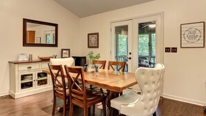 A dining area with a wooden table, six chairs, a white cushioned chair, a cabinet with dishes, a mirror, and framed pictures on the wall. - Cozy Retreat with Fireplace, Netflix & Easy Ramp Access - Deer View Retreat (Jasper)