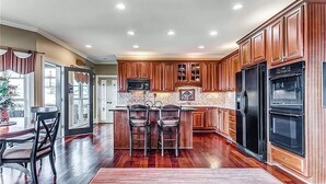 A kitchen with wooden cabinets, a central island with bar stools, a refrigerator, and a microwave. - Eagles View - Gorgeous Mountain Views + Luxury Interiors + Telescope + Library (Dawsonville)
