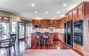 A kitchen with wooden cabinets, a central island with bar stools, a refrigerator, and a microwave.